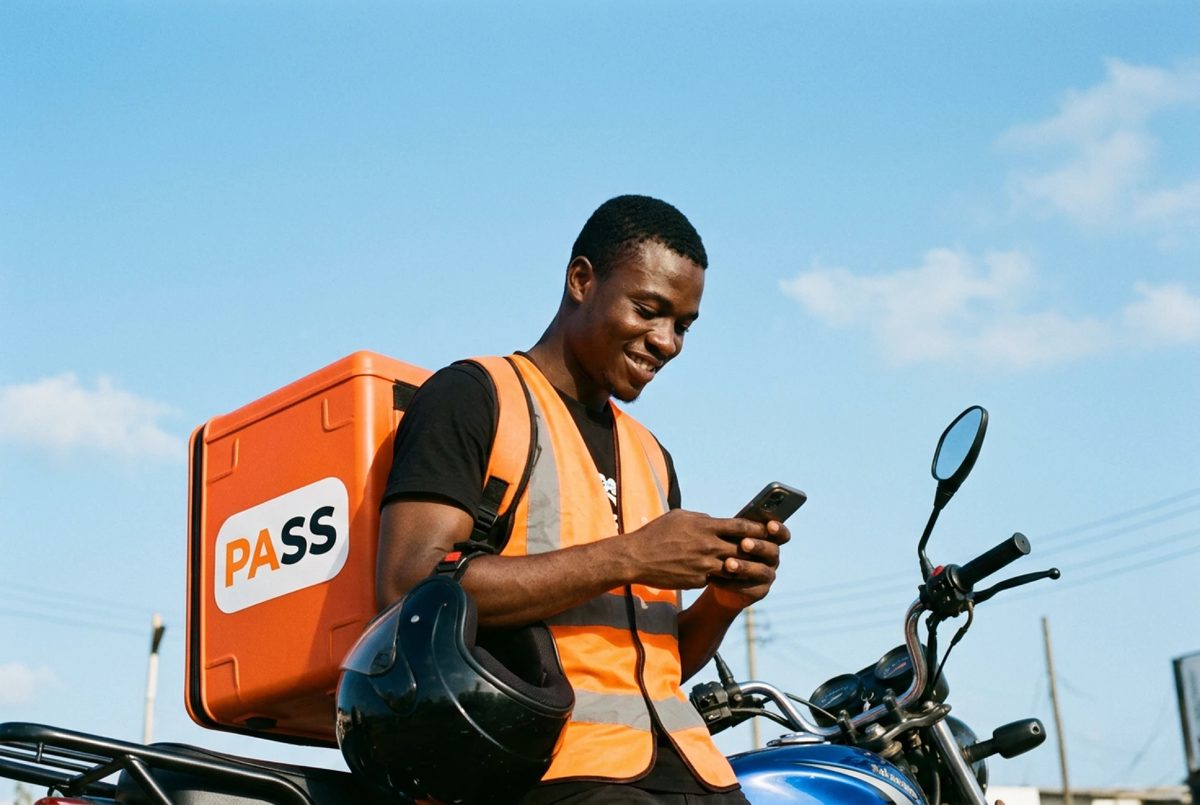 A PASS rider in an orange vest checks his phone, the orange PASS delivery box on his back